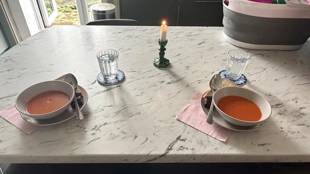 Two bowls of tomato soup and sandwiches set around a lit candle on the family lunch table.