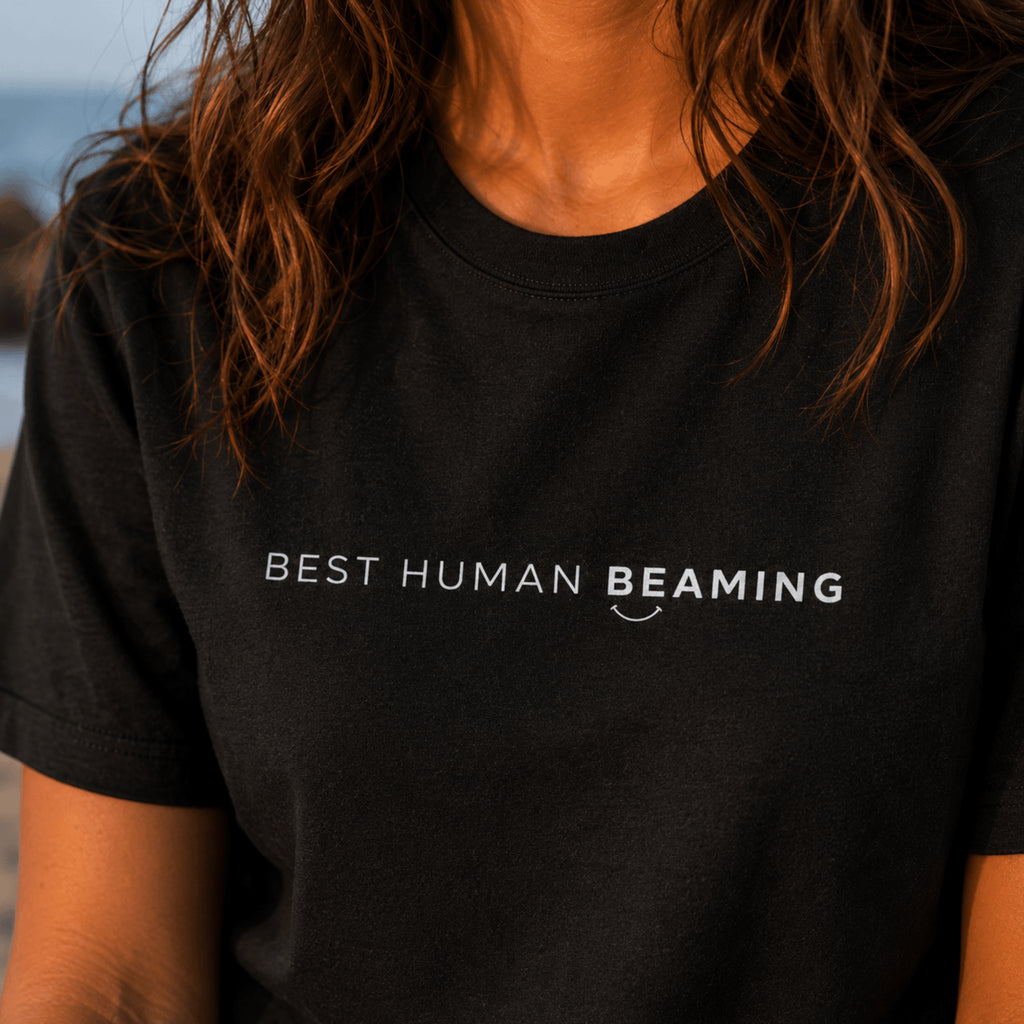 Close-up of the black Best Human Beaming organic cotton tee showing the white logo and fabric detail.