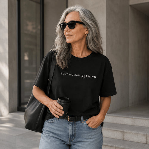 Older woman wearing the black Best Human Beaming unisex organic cotton tee with sunglasses and jeans.